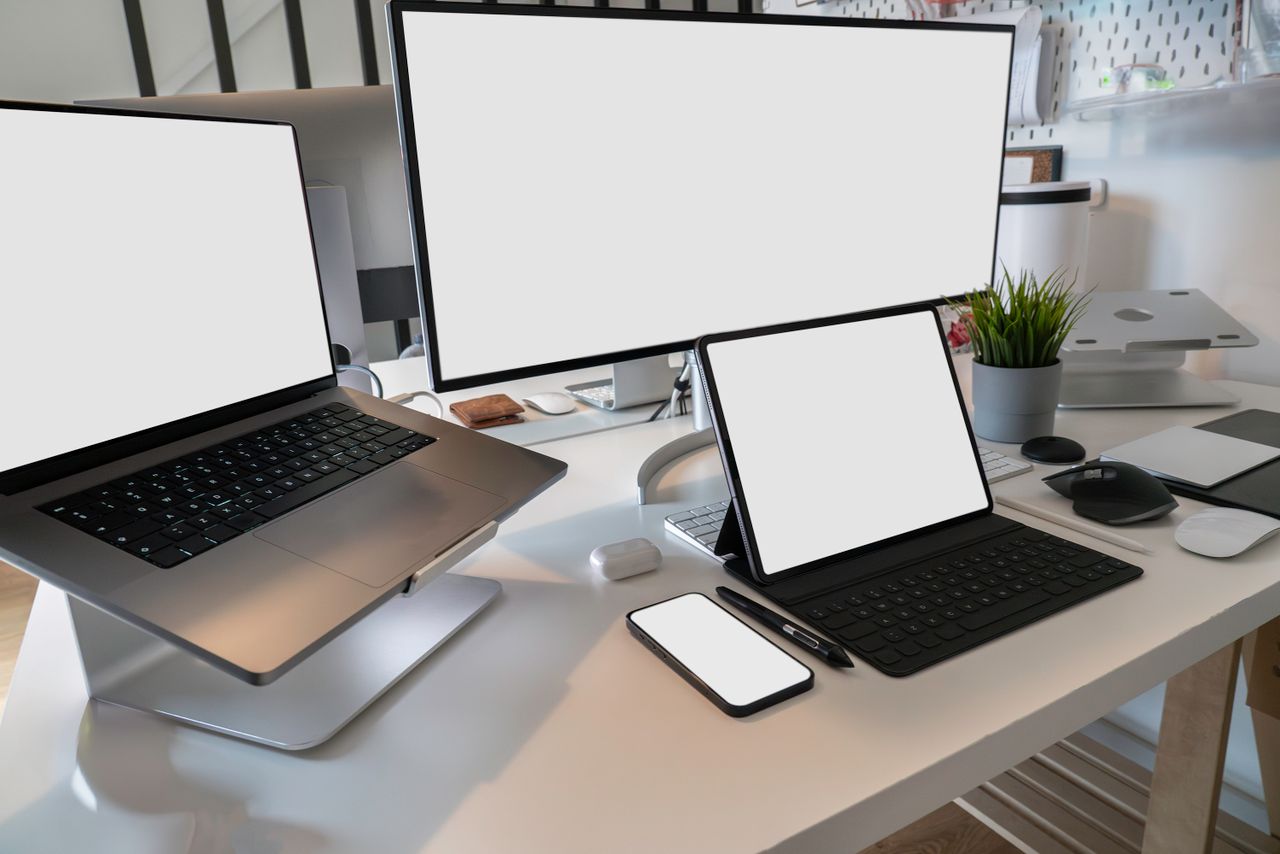 Un espace de travail propre et contemporain, avec un ordinateur portable, une tablette, un smartphone et un écran. Parfait pour le télétravail et les installations technologiques.