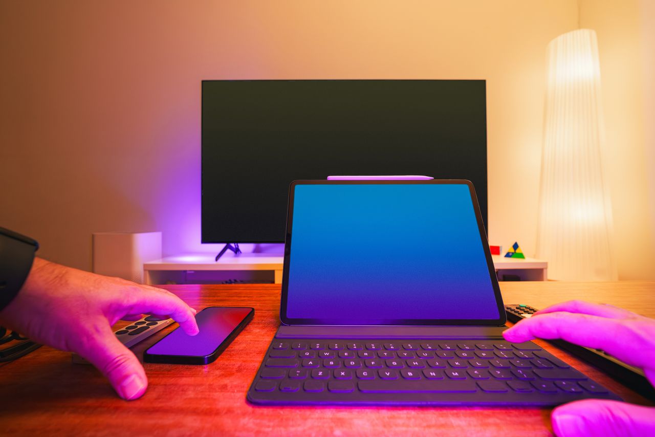 A lively workspace showing a laptop, tablet, and TV illuminated by colorful lighting.